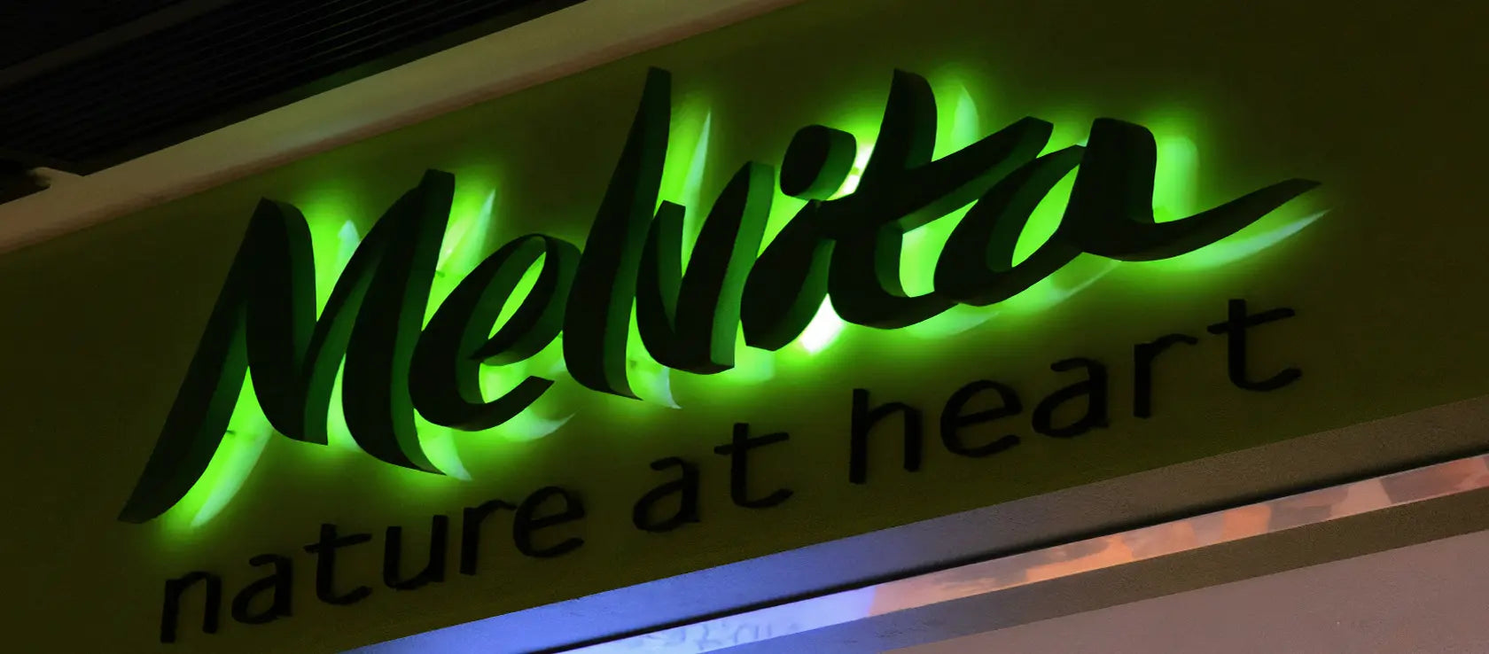 Green backlit script logo sign mounted on a storefront facade